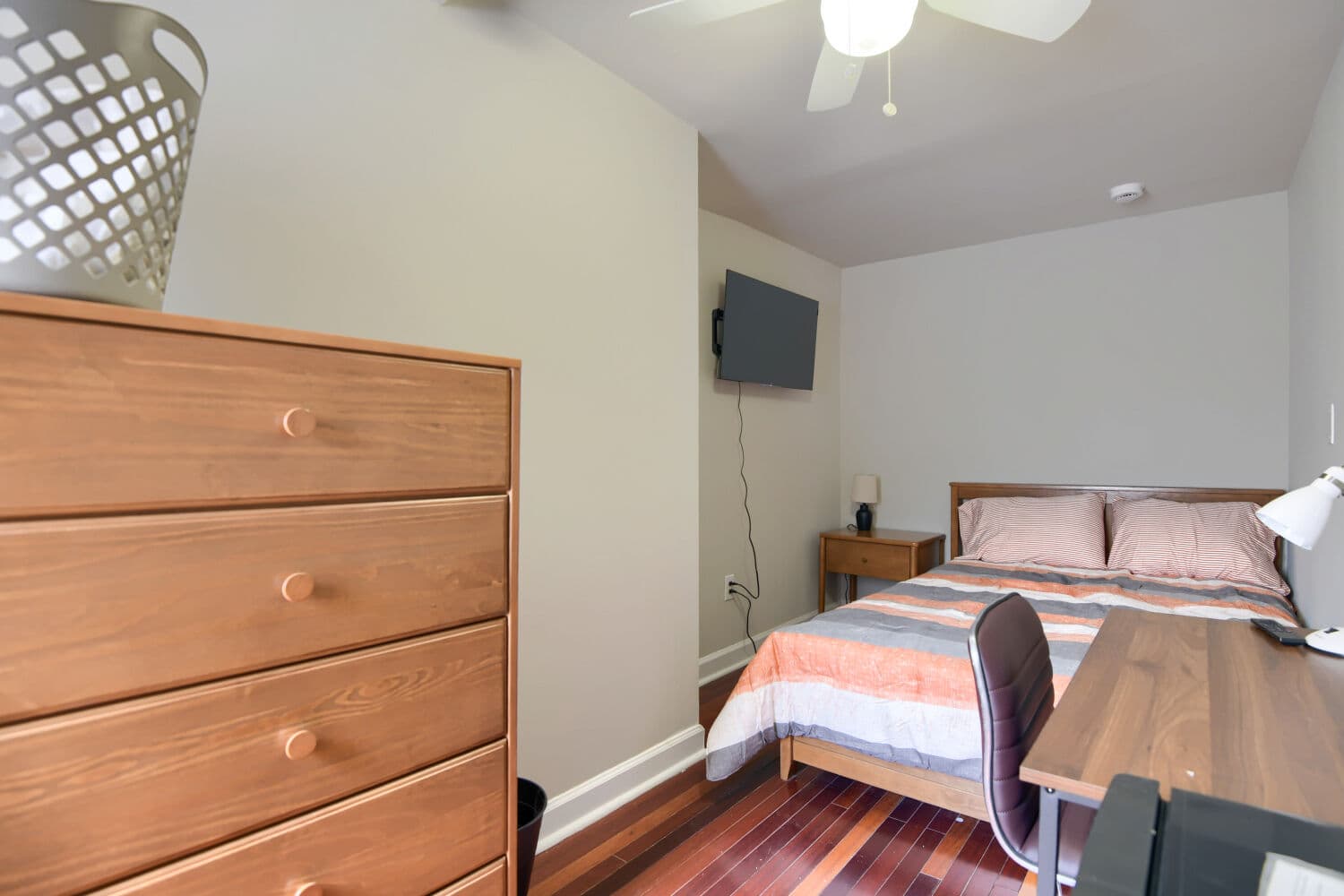 Furnished bedroom with wooden dresser, built-in desk with task chair, and hardwood floors